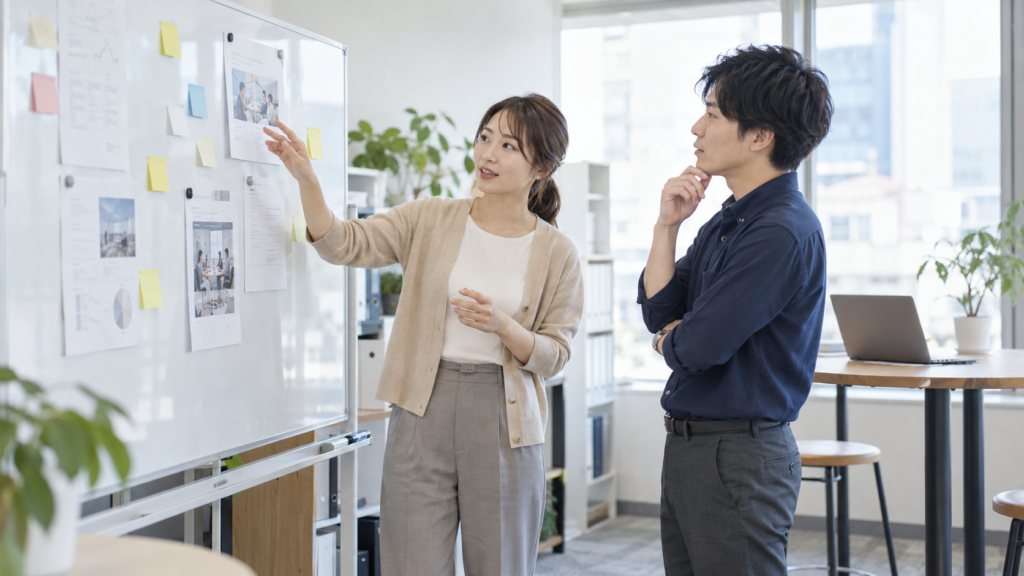 社員2人がホワイトボードの資料を見ながら採用業務について話し合う様子